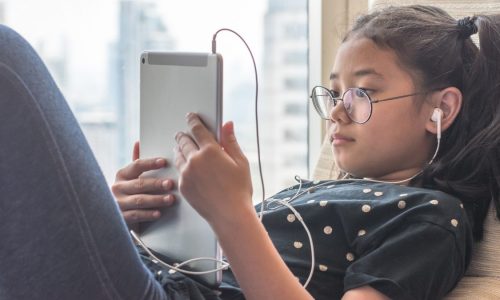 child reclining using an iPad and corded ear buds