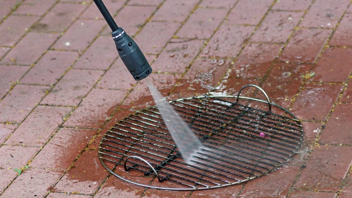 A person uses a pressure washer to clean the grates of an outdoor grill.