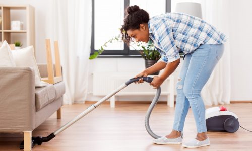 Woman using stick vacuum under her couch.