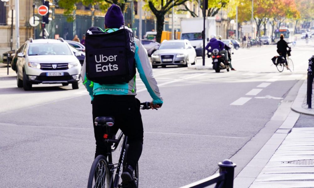 An Uber Eats delivery person rides a bike with the company's logo on their backpack.