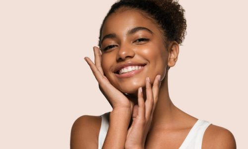 A woman smiles as she feels the skin on her face.