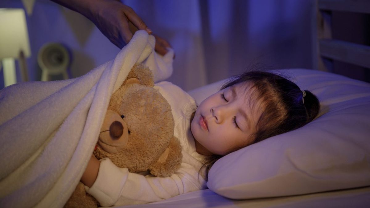 A mom puts a blanket on her sleeping child at bedtime.