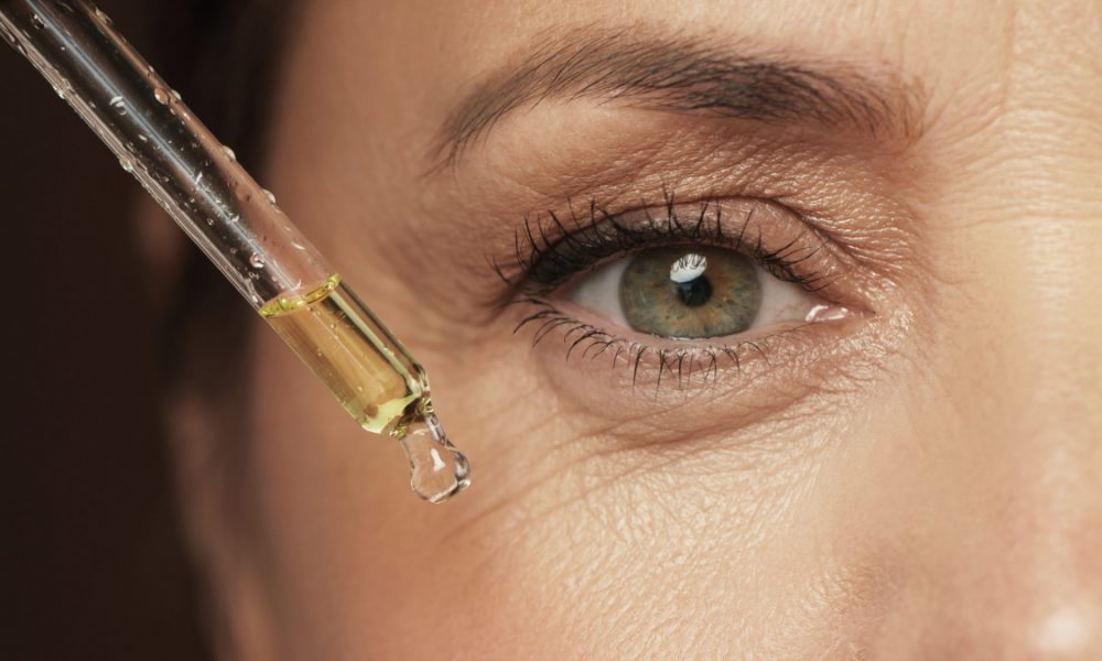 Woman uses vitamin C serum below eye for skin care.