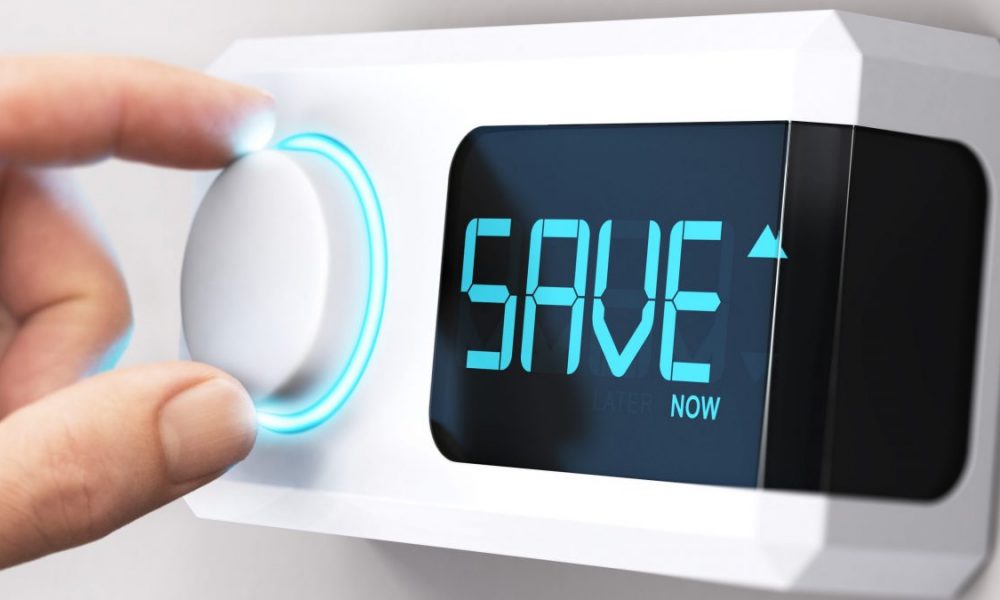 A hand turns a thermostat down with the word "Save" displayed on the readout.