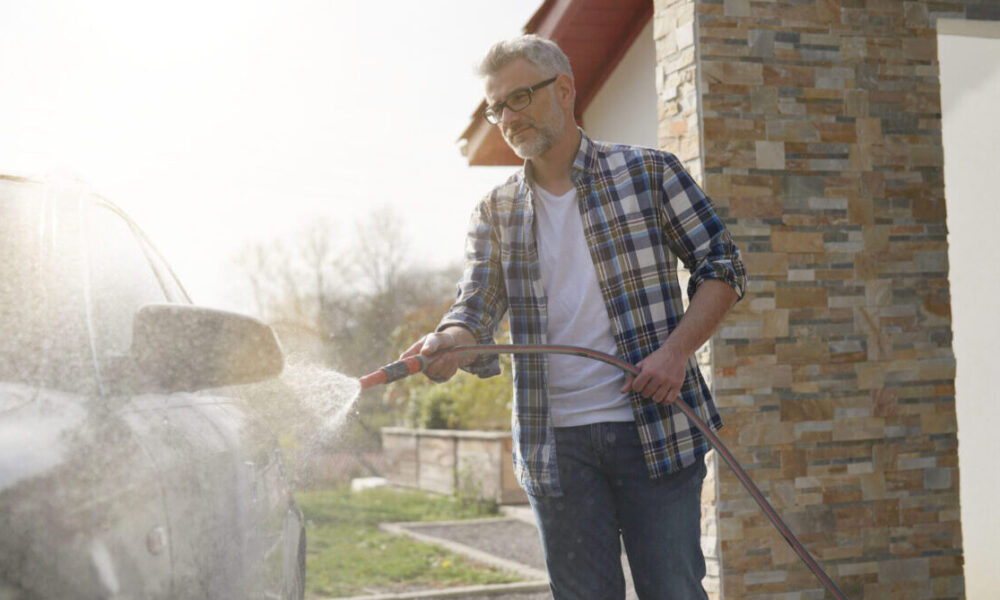 Mature man washing his car in driveway