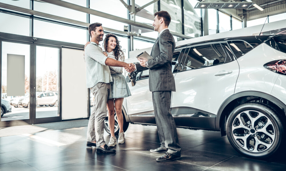 Young couple in a car dealership shaking hands with sales agent