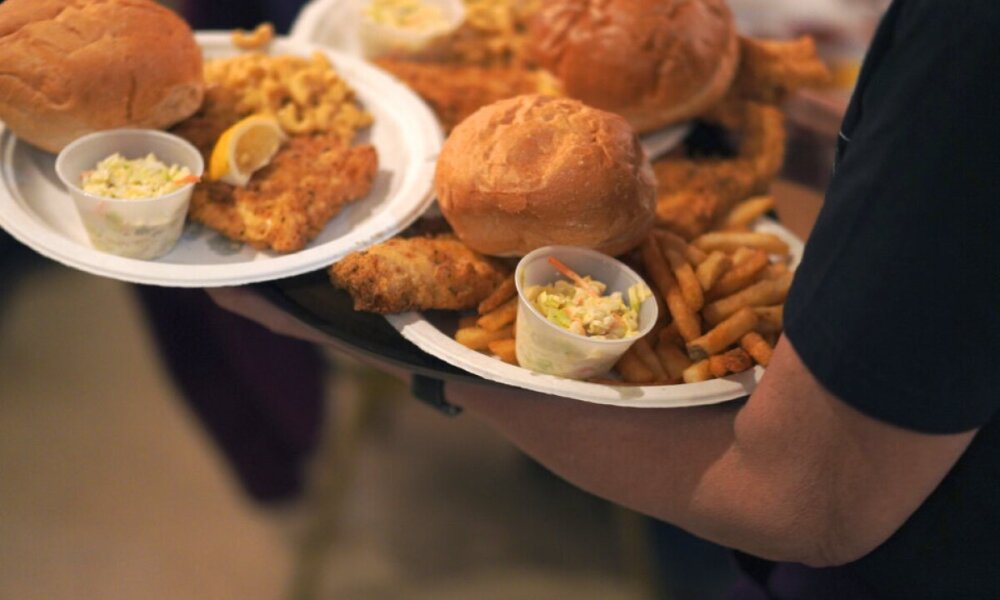 Person carries plates of fried fish sandwiches