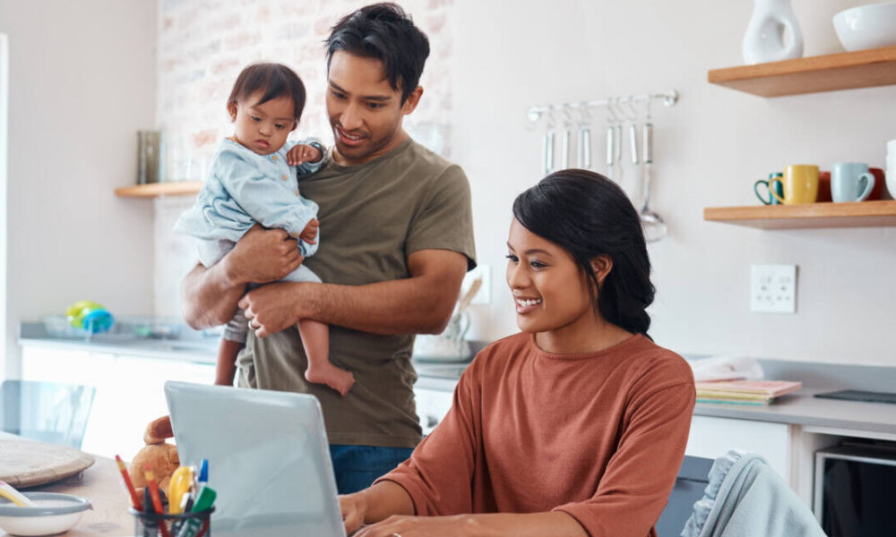 happy parents, dad holds baby while mom works