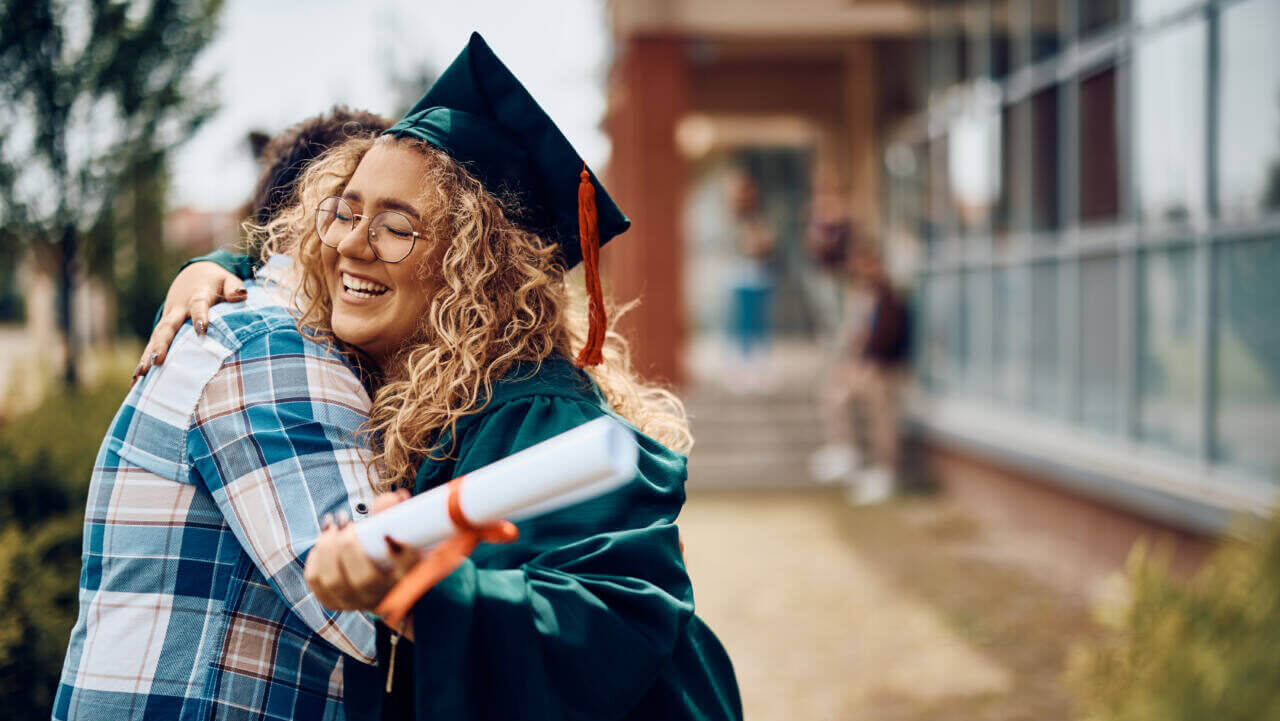 Happy graduate embraces father after graduation ceremony.